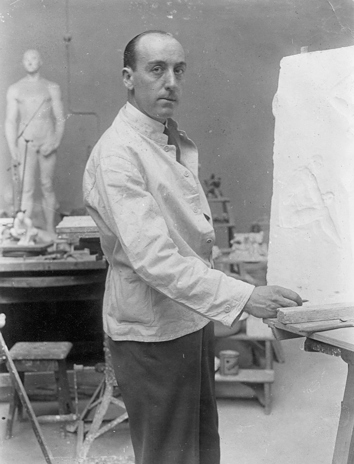 Edwin Scharff steht in seinem Berliner Atelier und blickt in die Kamera, 1923. Im Hintergrund steht die Plastik Der junge Athlet.
