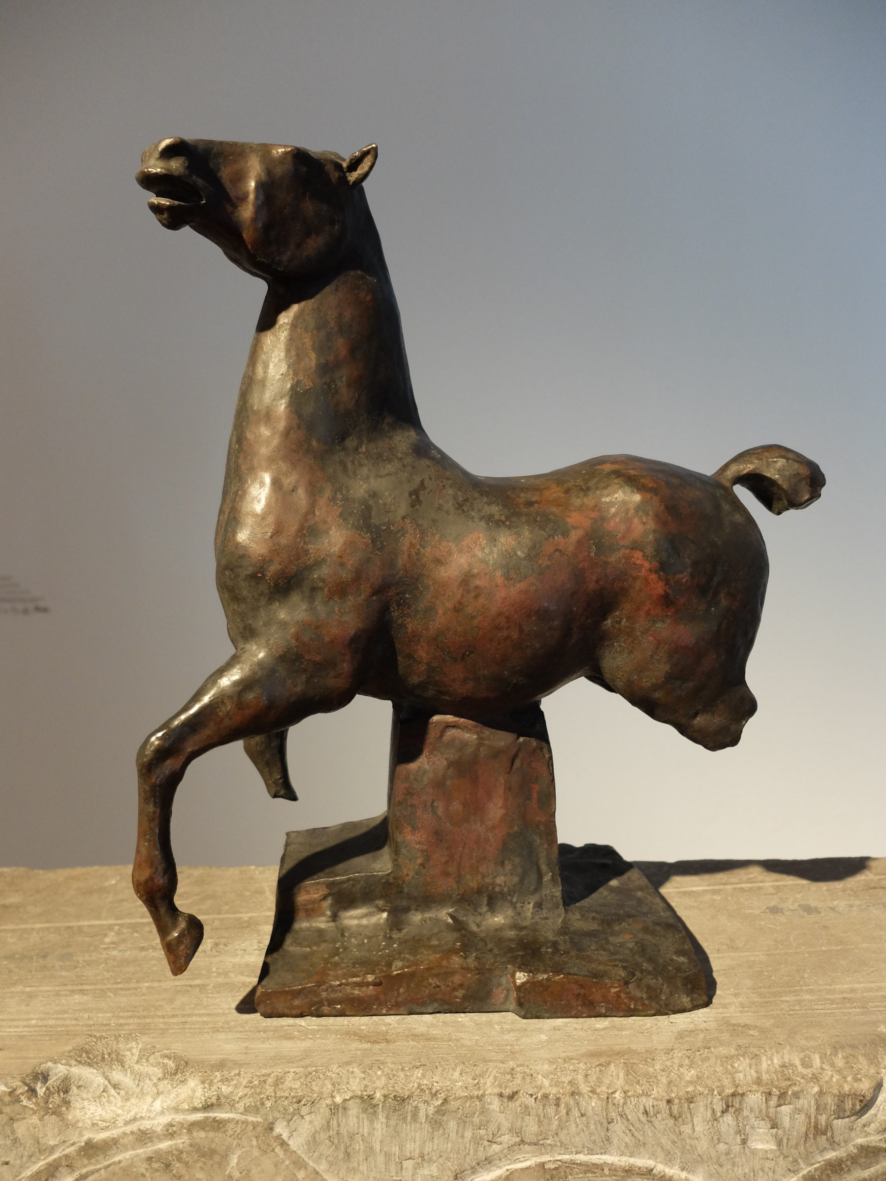 Das Foto zeigt das Denkmal der Pferde von Edwin Scharff, ein Kunstwerk aus Bronze. Das Pferd ist auf einen Steinsockel montiert. Dem Pferd fehlen die Hinterläufe und der rechte Vorderhuf.