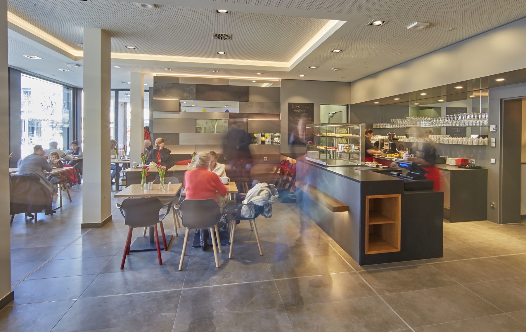 Im Museumscafé sitzen Menschen an den Tischen. Rechts im Foto ist die Cafetheke mit der Kasse. Hier kann man auch aus verschiedenen Kuchen auswählen.