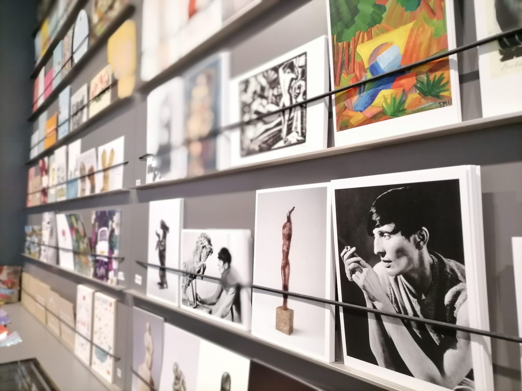 Das Foto zeigt die Postkartenwand im Museumsshop. Es gibt sowohl Postkarten zur Kunst und den Ausstellungen als auch lustige Karten oder Karten für bestimmte Anlässe.