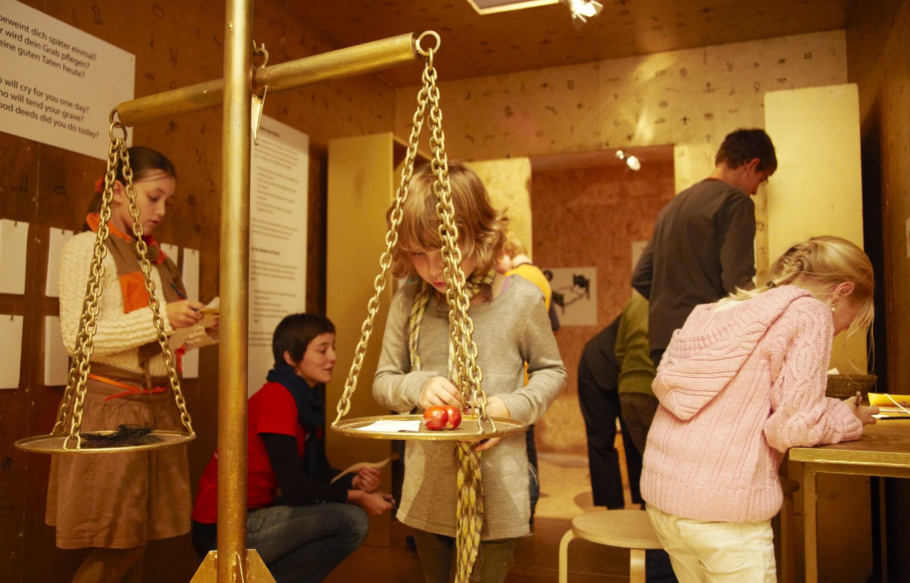 Kinder entdecken die Ausstellung Erzähl mir was vom Tod. Sie stehen vor einer Waage, Es geht um die Seele und ob man das Leben wiegen kann. Im Reich des Osiris - hier kann man sich auf das Leben nach dem Tod vorbereiten.