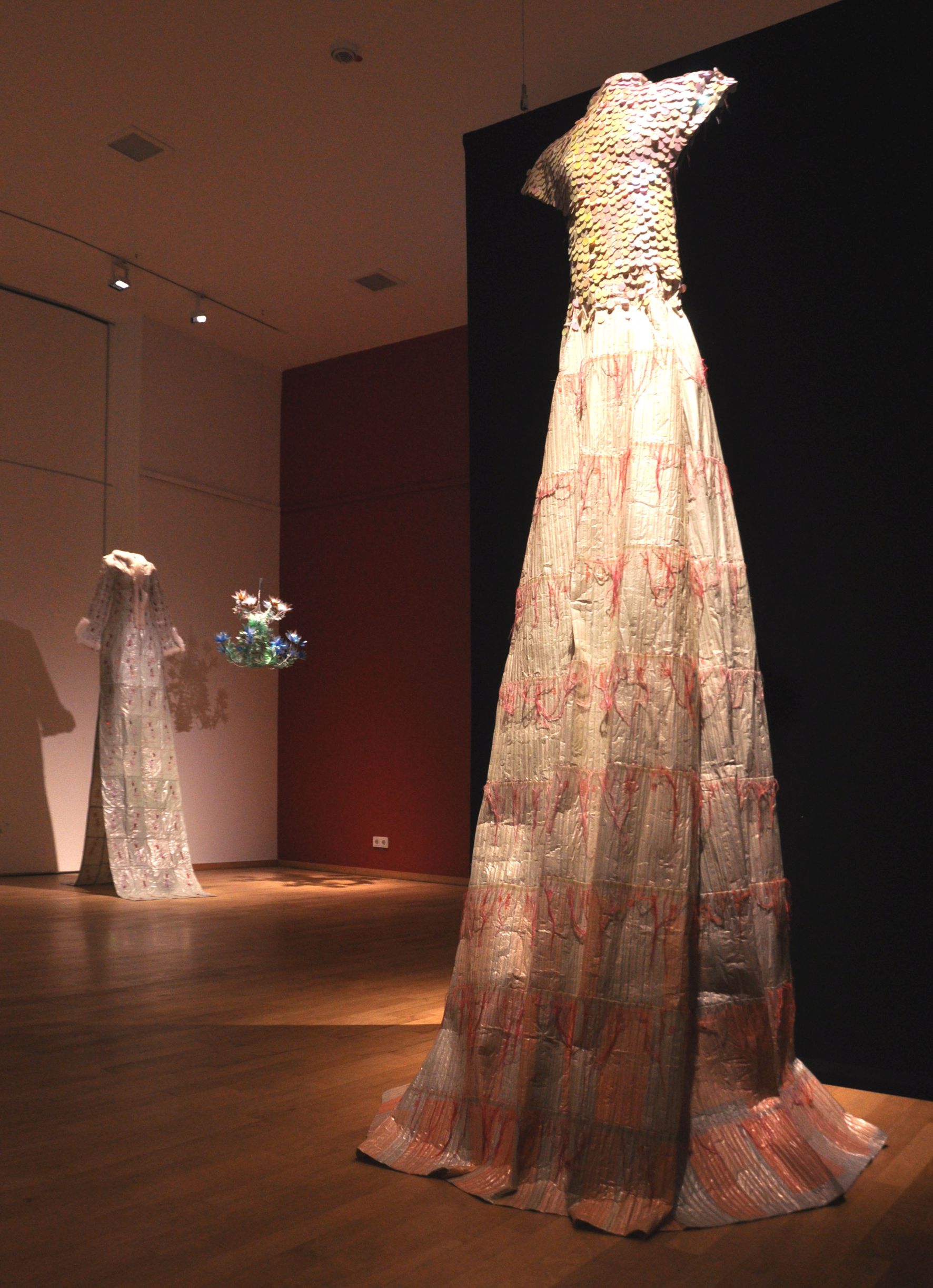 Auf dem Foto ist ein sehr schickes Kleid in einem Ausstellungsraum zu sehen. Es hängt von der Decke herunter. Es besteht aus wiederverwendeten Materialien.